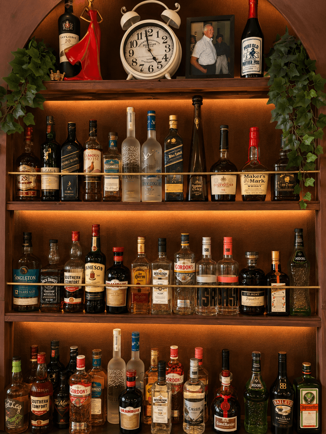Warmly lit wooden shelves filled with liquor bottles, featuring a large clock and hanging ivy.