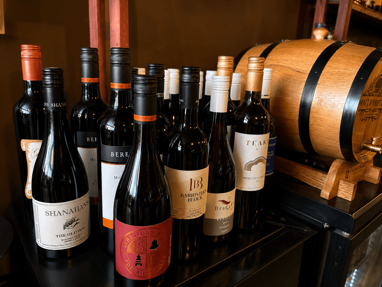 Assorted wine bottles from various brands standing beside a small wooden barrel.