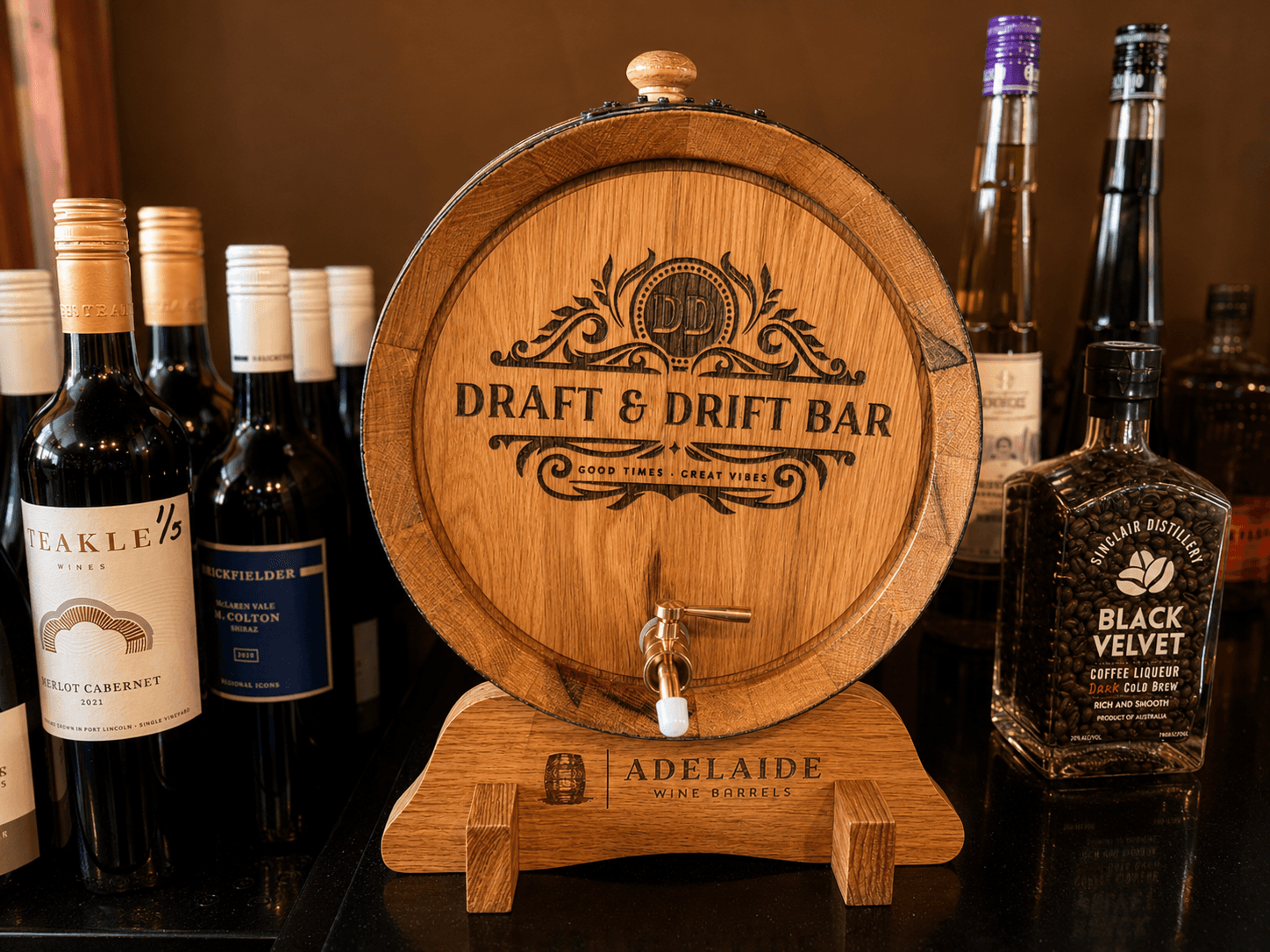 Wooden wine barrel labeled 'Draft & Drift Bar' surrounded by wine and coffee liqueur bottles.