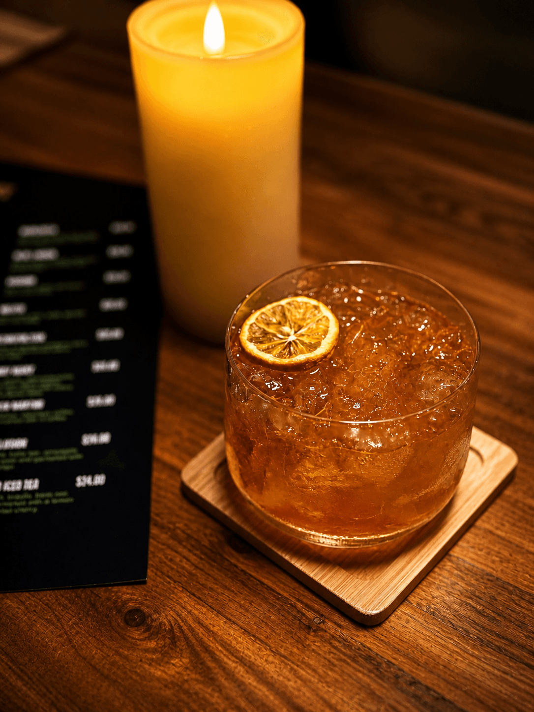 Amber cocktail with crushed ice and dried orange garnish beside a glowing candle.